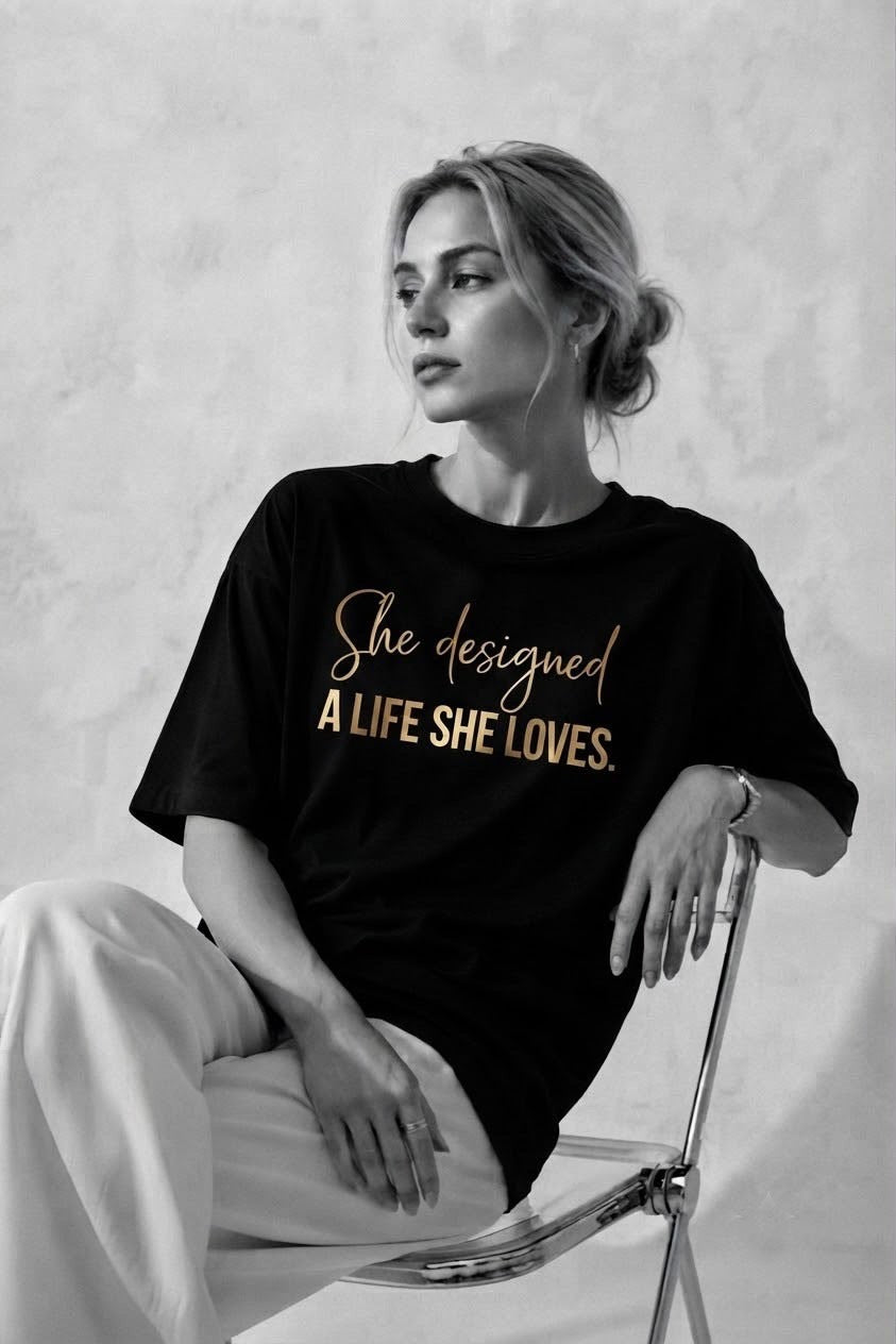 Woman wearing the black A Life She Loves oversized tee with the gold She designed a life she loves print