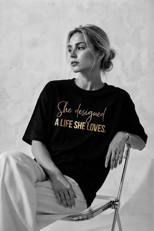 Woman wearing the black A Life She Loves oversized tee with the gold She designed a life she loves print