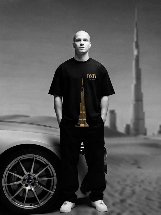 Man wearing the black City of Dreams oversized tee with the gold DXB Est. 1971 Burj Khalifa front print