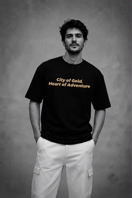 Man wearing the black City of Gold Heritage oversized tee with the gold City of Gold, Heart of Adventure front print