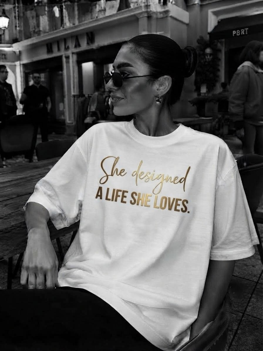 Woman wearing the white A Life She Loves oversized tee with the gold She designed a life she loves print