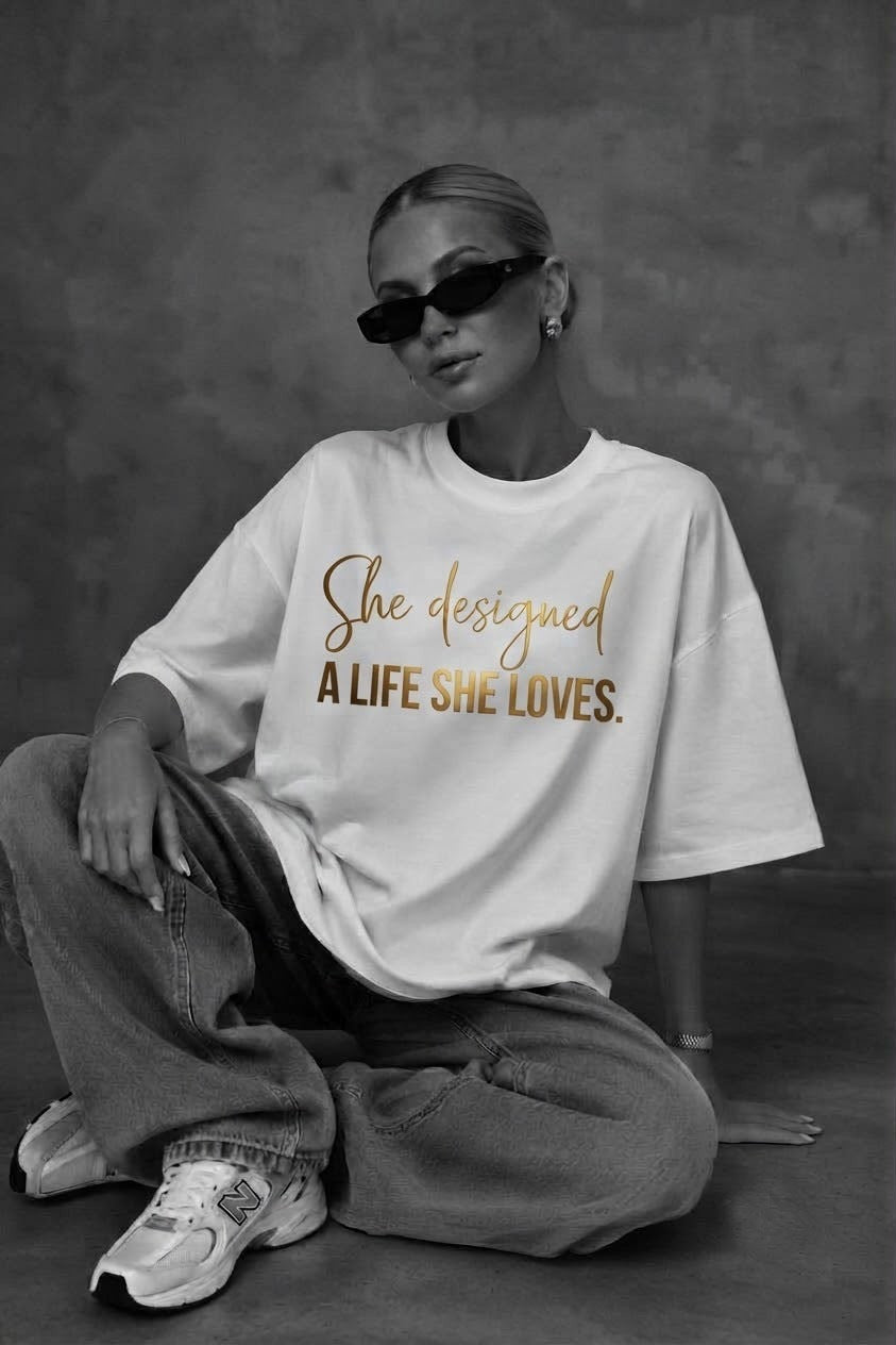 Woman sitting in the white A Life She Loves oversized tee with gold script print